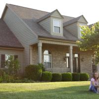 woman sitting on her large lawn with her dog next to her in front of their home