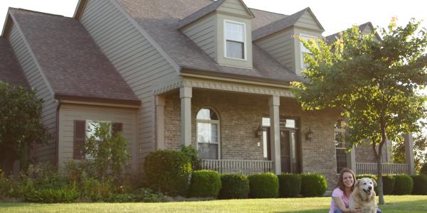 woman sitting on her large lawn with her dog next to her in front of their home